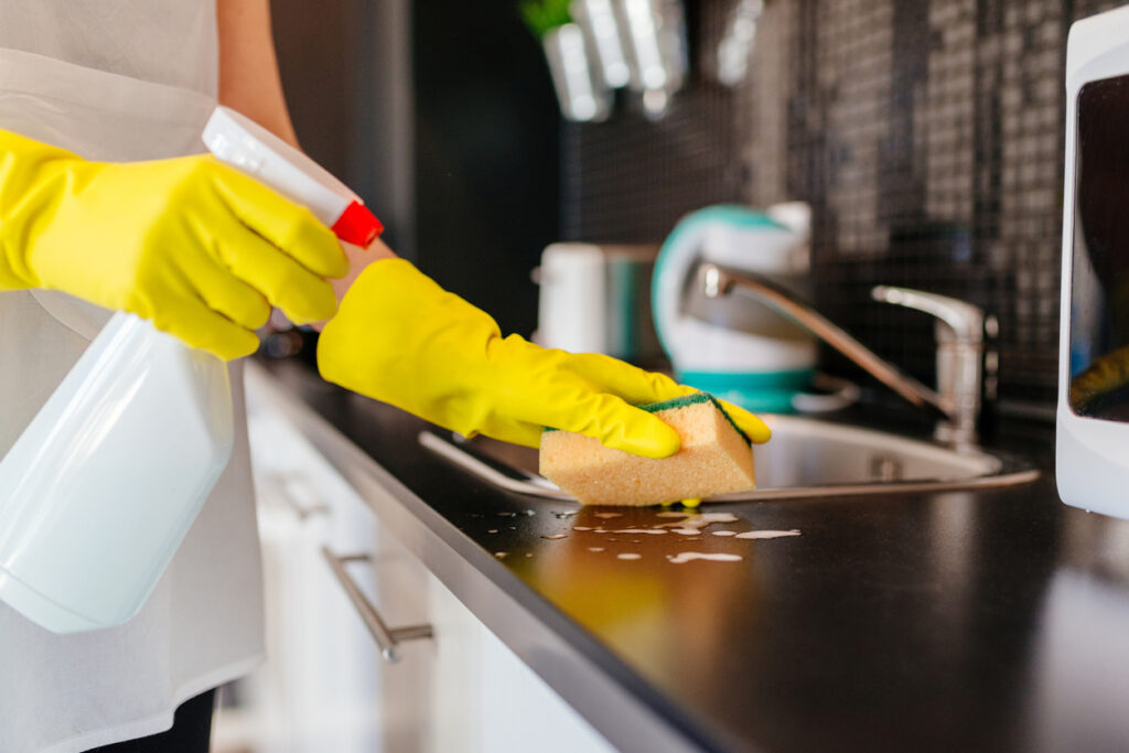 woman cleaning kitchen cabinets with sponge and spray cleaner